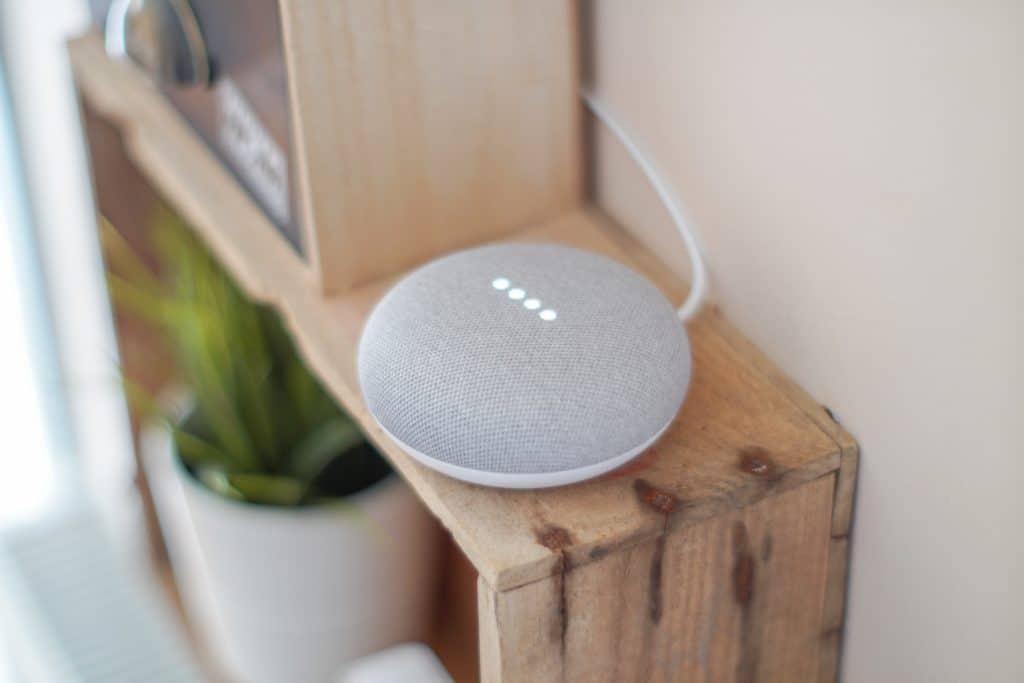 A Google Home Mini device placed on a wooden shelving unit
