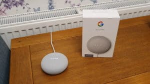 The Google Nest Mini (2nd generation) on a table, processing the command "Ok Google, play Skies and Shadows"